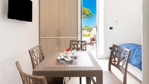 Une pièce comprenant une table à manger dressée pour quatre personnes, un téléviseur fixé au mur et une porte donnant sur un espace extérieur avec vue sur la verdure.