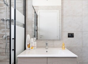 A bathroom with a glass shower enclosure, a white sink, and toiletries. - Monolocale Vela – Nuovo con Wi-Fi, Clima e Giardino a Torre Lapillo (Nardò)