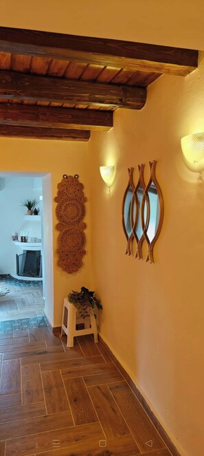 A hallway with wooden flooring, a white wall with decorative wall art, and a small white stool with a plant. - Peaceful village stay (Karousades)