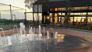 Uma fonte com vários jatos, rodeada por um espaço pavimentado com borda de tijolos.