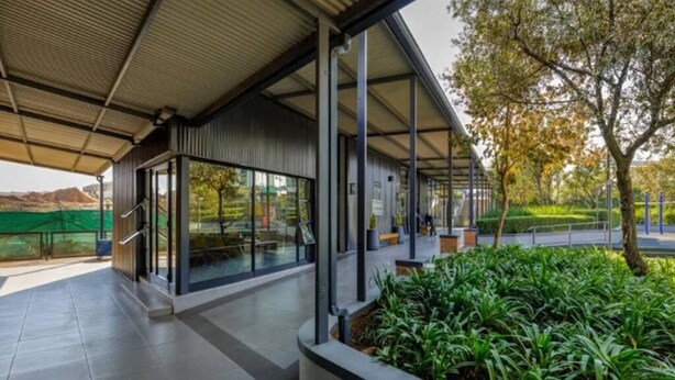 Um edifício moderno com entrada coberta, portas de vidro e área ajardinada com plantas.