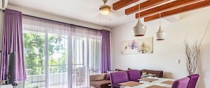 A modern living room with a glass dining table, purple sofas, and a large window with sheer curtains. - Infiniti Blu Family suite with private beach! (sosua, puerto plata)