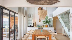 A modern dining area with a wooden table and chairs, a hanging light fixture, and a staircase leading to an upper level. - Camps Bay Luxury Family Villa with Ocean Views (Cape Town)