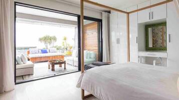A bedroom with a large bed, a TV, and a sliding glass door leading to a balcony with outdoor seating.