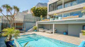 A modern building with a swimming pool, outdoor seating, and a mountain view.