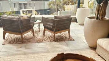 A covered outdoor seating area with wicker furniture, a wooden coffee table, and potted plants.