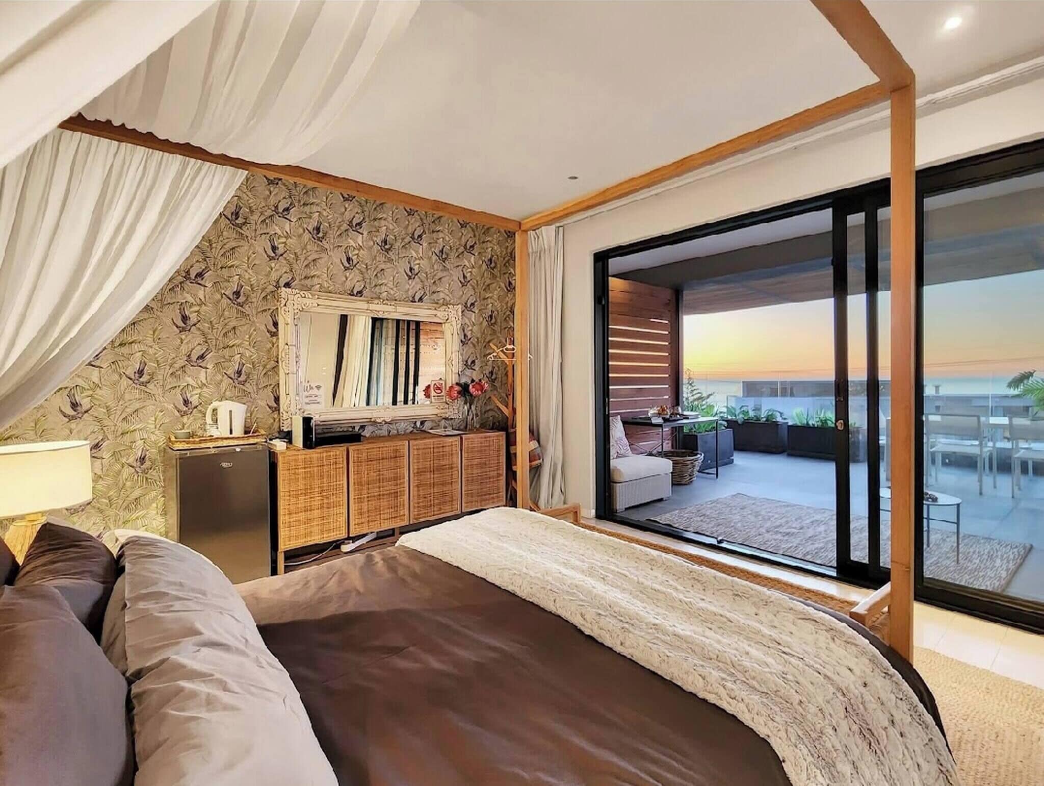 A bedroom with a large bed, a dresser, a mirror, and a balcony with a view.