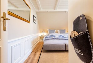 Ein Schlafzimmer mit Bett, Nachttisch, Lampe, Spiegel und einem an der Wand befestigten Staufach.