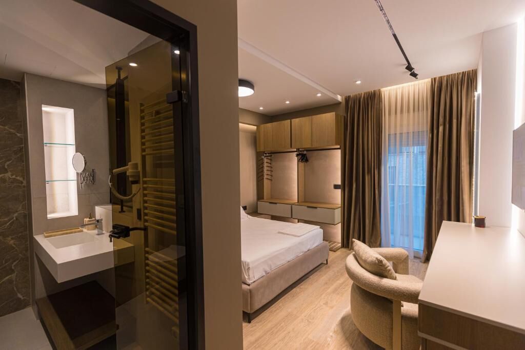 Una camera d'albergo moderna con un letto, una scrivania, una sedia, un angolo trucco con specchio e un armadio.
