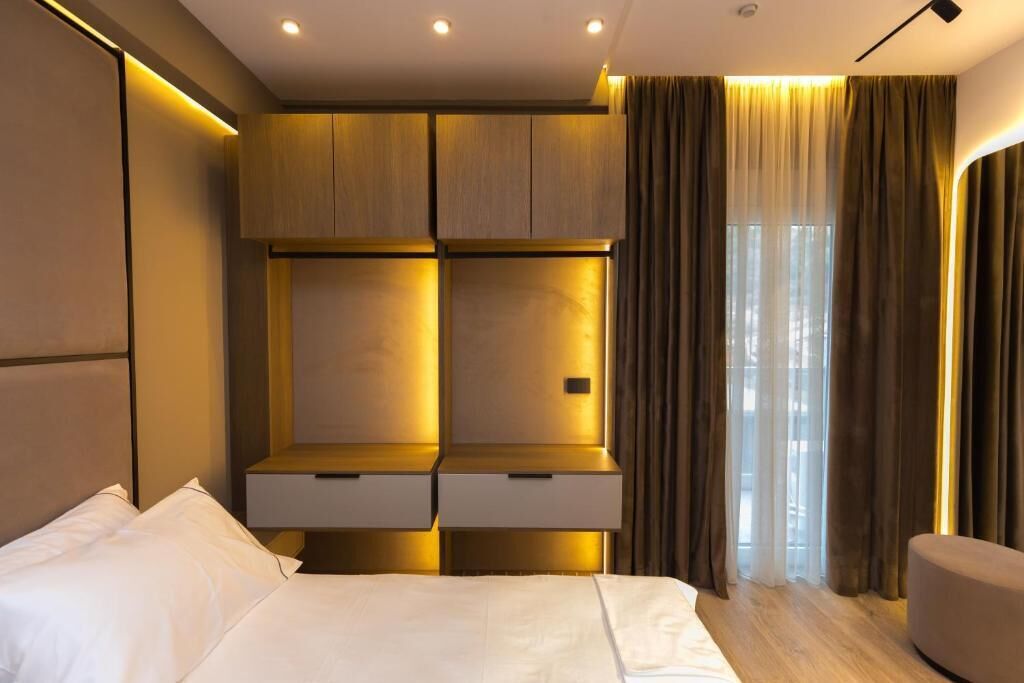 Una camera d'hotel moderna con un letto, spazio contenitori integrato, un'area salotto e un'ampia finestra con tende.
