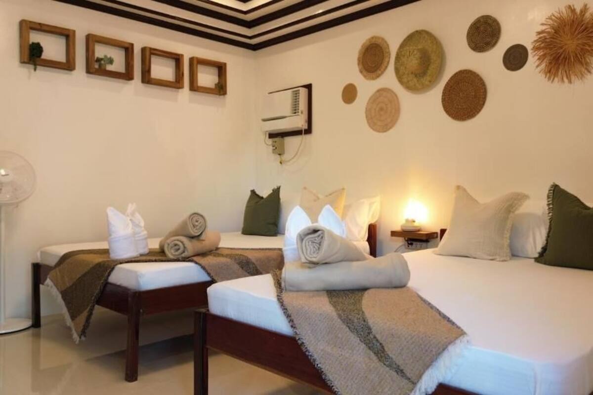 A hotel room with two beds, a bedside table, a wall-mounted air conditioner, and decorative wall art.