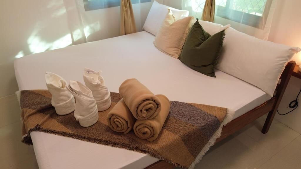 Una cama bien hecha con toallas enrolladas, una manta y almohadas.