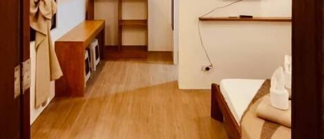 A compact hotel room with a wooden floor, a bed, a small desk, and a television mounted on the wall.