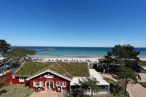 Ein Küstenhotel mit rotem Gebäude, einem grasbewachsenen Dach und Blick auf Strand und Meer.