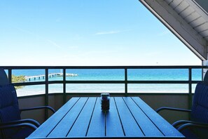 Ein Tisch mit einer Flasche, zwei Stühle und Blick auf das Meer sowie ein Steg im Hintergrund.