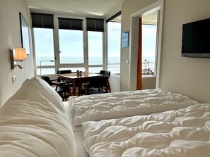 A hotel room with a bed, a table with chairs, a TV, and a view of the sea. - Al Mare - Modern apartment with balcony, sea view, parking space, WLAN. Pets (List auf Sylt)