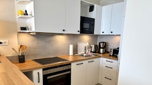 Uma cozinha moderna com armários brancos, um micro-ondas Bosch preto, um forno Siemens, bancada de madeira e uma cafeteira.
