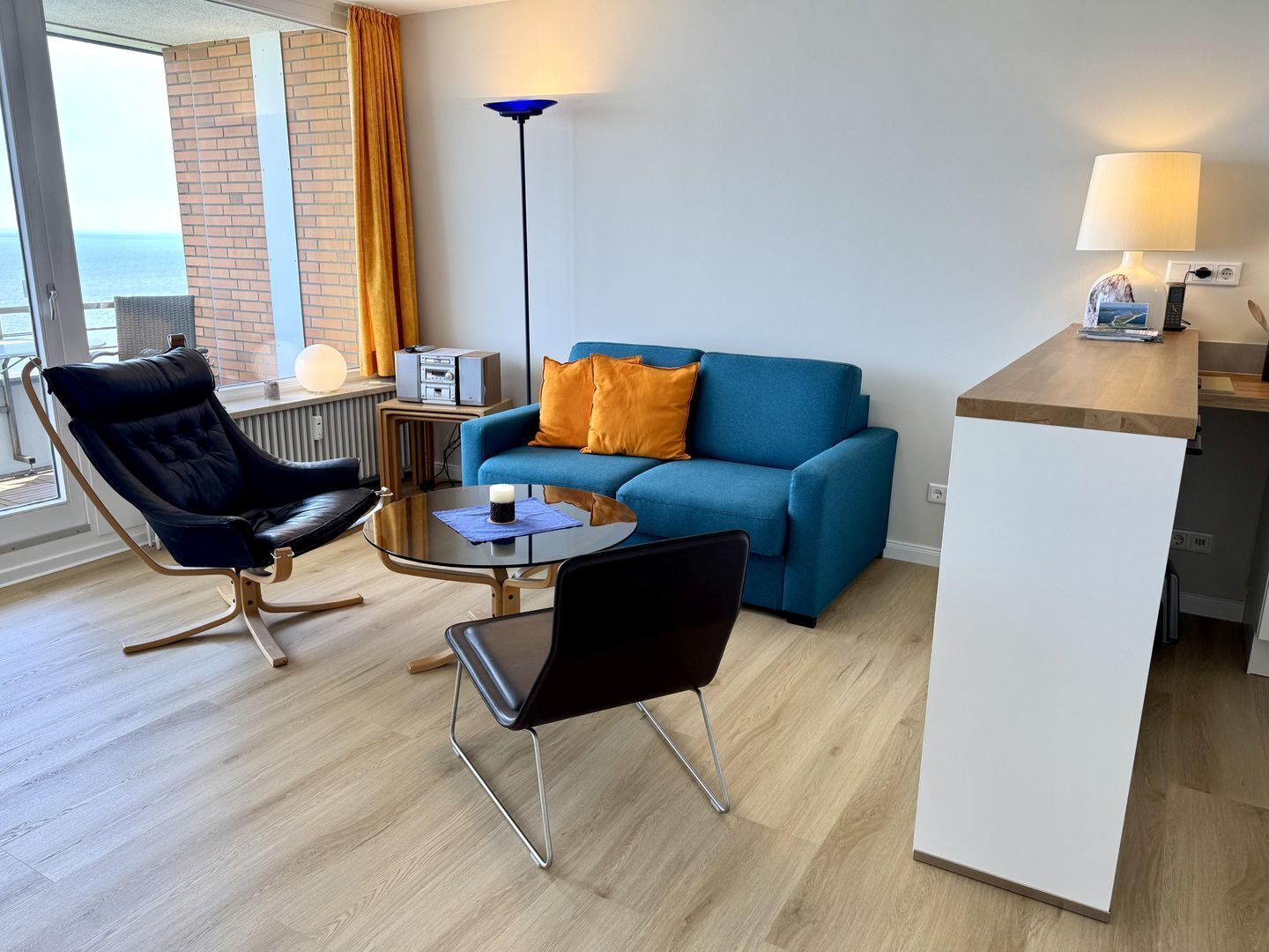 Een moderne woonkamer met een blauwe bank, een zwarte lederen fauteuil, een klein rond tafeltje en een lamp.