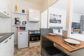 Een compacte keuken met een magnetron, koffiezetapparaat en oven, een eethoek met tafel en stoelen, en een groot raam met uitzicht op zee.
