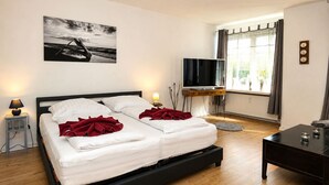 A bedroom with a bed, bedside lamps, a TV, a window with curtains, and a painting on the wall. - fewo1846 - Koje Sansibar - fewo1846 - Koje Sansibar / centrally located (Flensburg)
