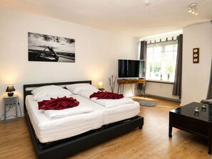 Een slaapkamer met een bed, nachtlampjes, een televisie, een raam met gordijnen en een schilderij aan de muur.