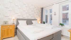 Un dormitorio con cama, mesitas de noche, una ventana y una pared decorada con motivos náuticos.