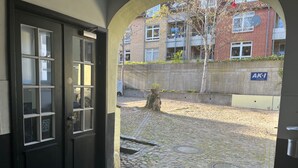 Un patio empedrado con una puerta negra, una pared de hormigón y un edificio con un cartel que dice 'AKI Immobilien' al fondo.