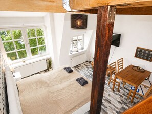 Ein Schlafzimmer mit Bett, Fenster, Heizkörper, Fernseher und einem Essbereich mit Tisch und Stühlen.