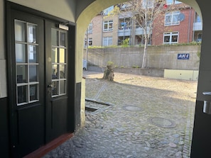 A cobblestone courtyard with a black door, a concrete wall, and a building with a sign 'AKI Immobilien' in the background.