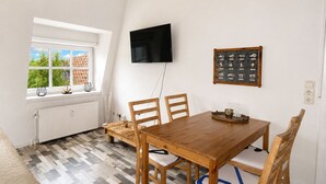 Ein Essbereich mit Holztisch und Stühlen, einem an der Wand befestigten Fernseher und einem Fenster mit Blick auf ein Dach.
