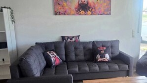 Un salon moderne avec un canapé d’angle, une table basse et un tableau coloré accroché au mur.