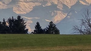 Une chaîne de montagnes aux sommets enneigés, un paysage verdoyant au premier plan et un ciel dégagé.