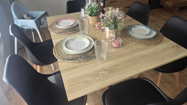 Un coin repas avec une table dressée pour quatre personnes, entouré de chaises noires, d’un téléviseur et d’un meuble en bois.