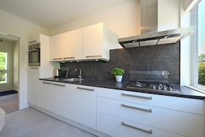 A modern kitchen with white cabinets, a black countertop, a stainless steel range hood, and a gas stove. - Enjoy comfort, tranquility and waterside living at Zilt&Zalig on Oranjeplaat. Modern holiday home with private jetty near Lake Veere in Zeeland (Arnemuiden)