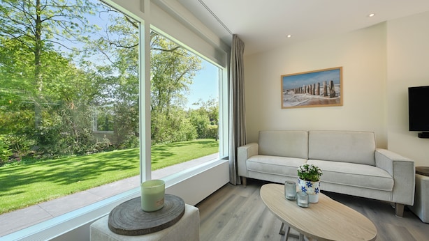 A modern living room with a large window, a sofa, a coffee table, and a painting on the wall. - Holiday home close to the water, with a private berth at the jetty, quiet location (Arnemuiden)
