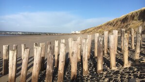 A beach with wooden posts, a dune, and a pier in the background. - Holiday home close to the water, with a private berth at the jetty, quiet location (Arnemuiden)