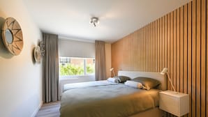 A modern bedroom with a large bed, bedside tables, a window with curtains, and a wooden wall panel. - Holiday home close to the water, with a private berth at the jetty, quiet location (Arnemuiden)