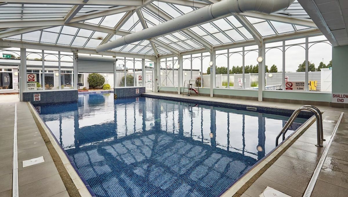 Una piscina interior con techo de cristal, agua cristalina y zonas marcadas, una poco profunda y otra profunda.