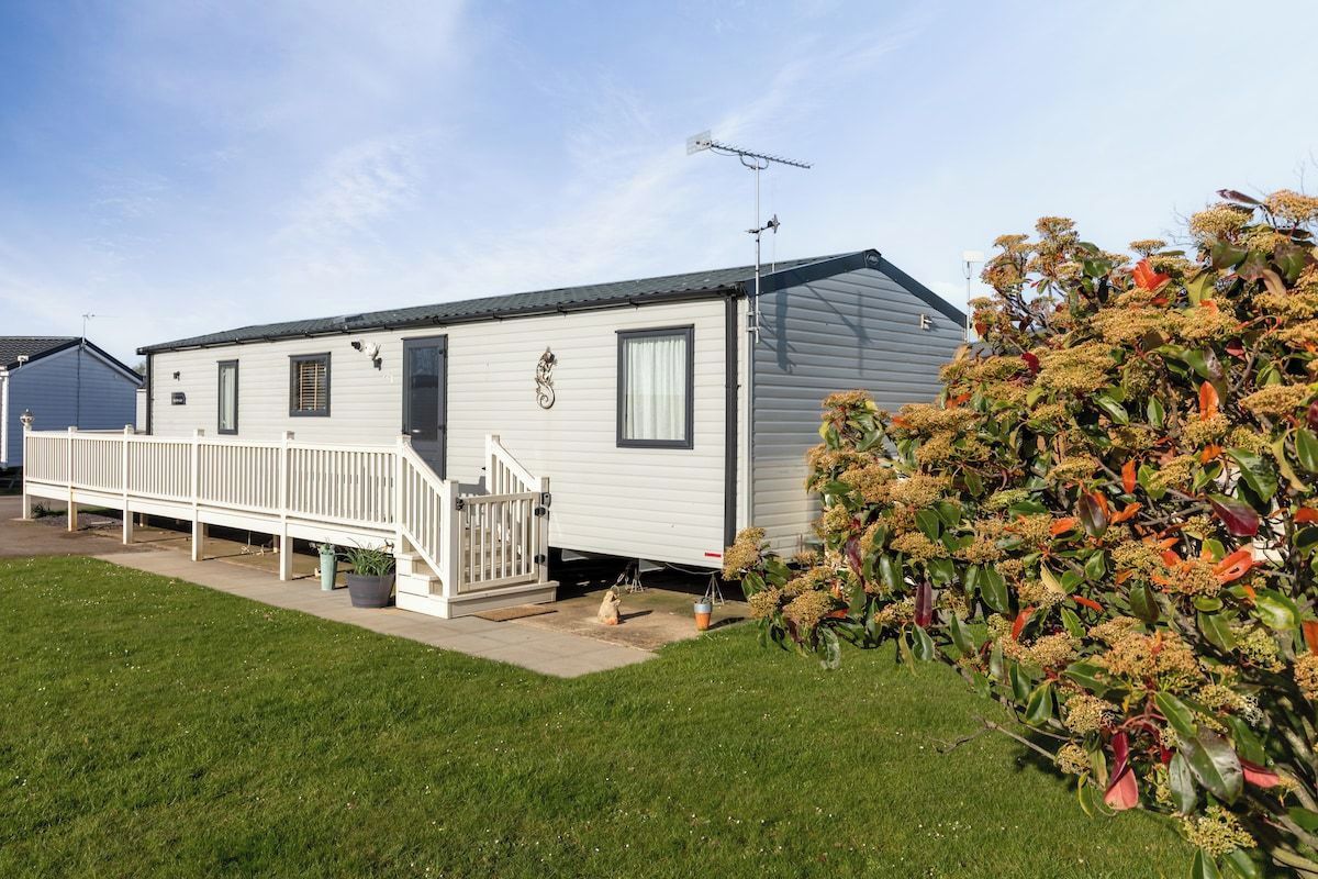 A mobile home with a porch, a small staircase, and a garden with flowering plants.