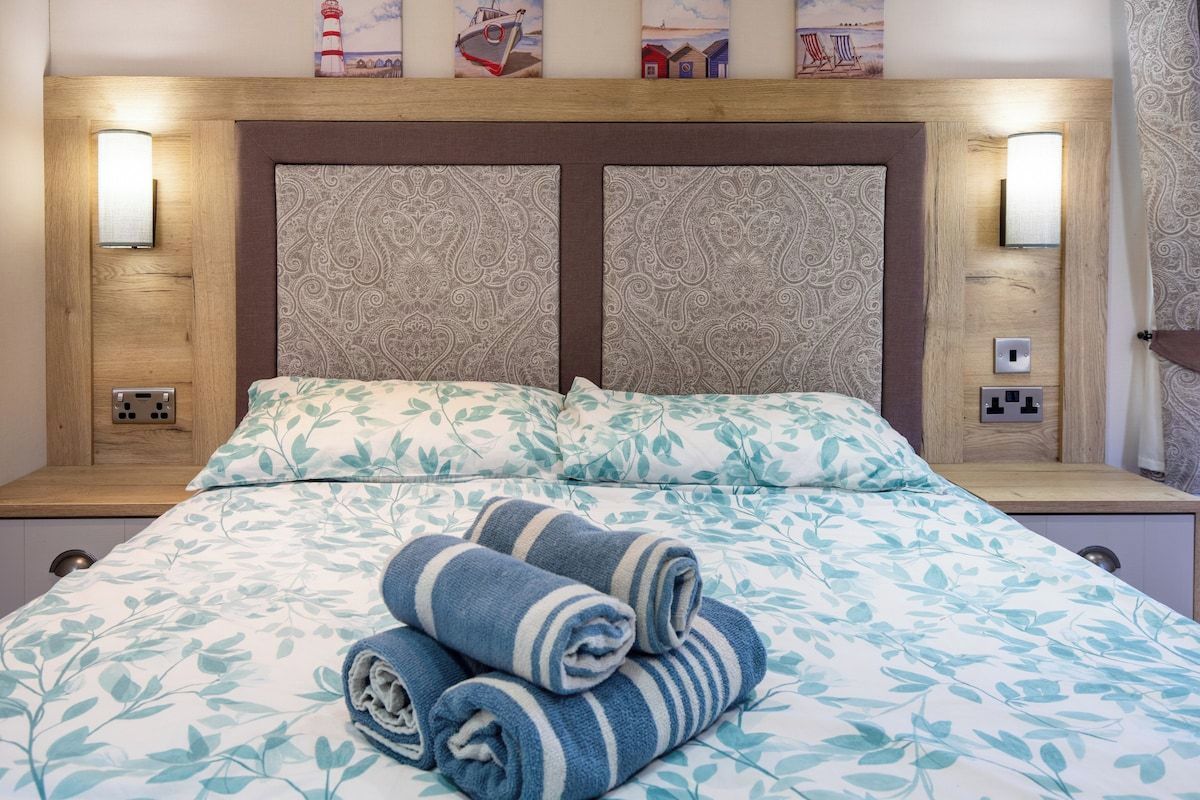 Une chambre d’hôtel avec un lit, deux lampes de chevet et une tête de lit ornée d’un motif décoratif.