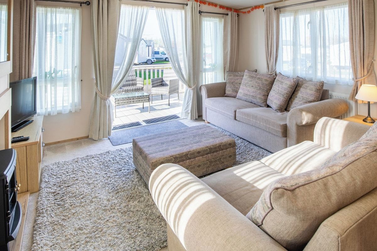 Una sala de estar con sofá, reposapiés y televisor sobre un mueble.