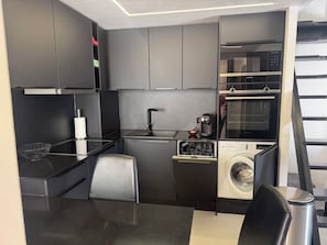Eine kompakte Küche mit integrierter Waschmaschine, einer Kaffeemaschine und einer Mikrowelle.