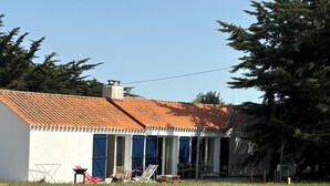 A small building with a tiled roof, a white exterior, and blue shutters. There are outdoor chairs and a picnic table in front.