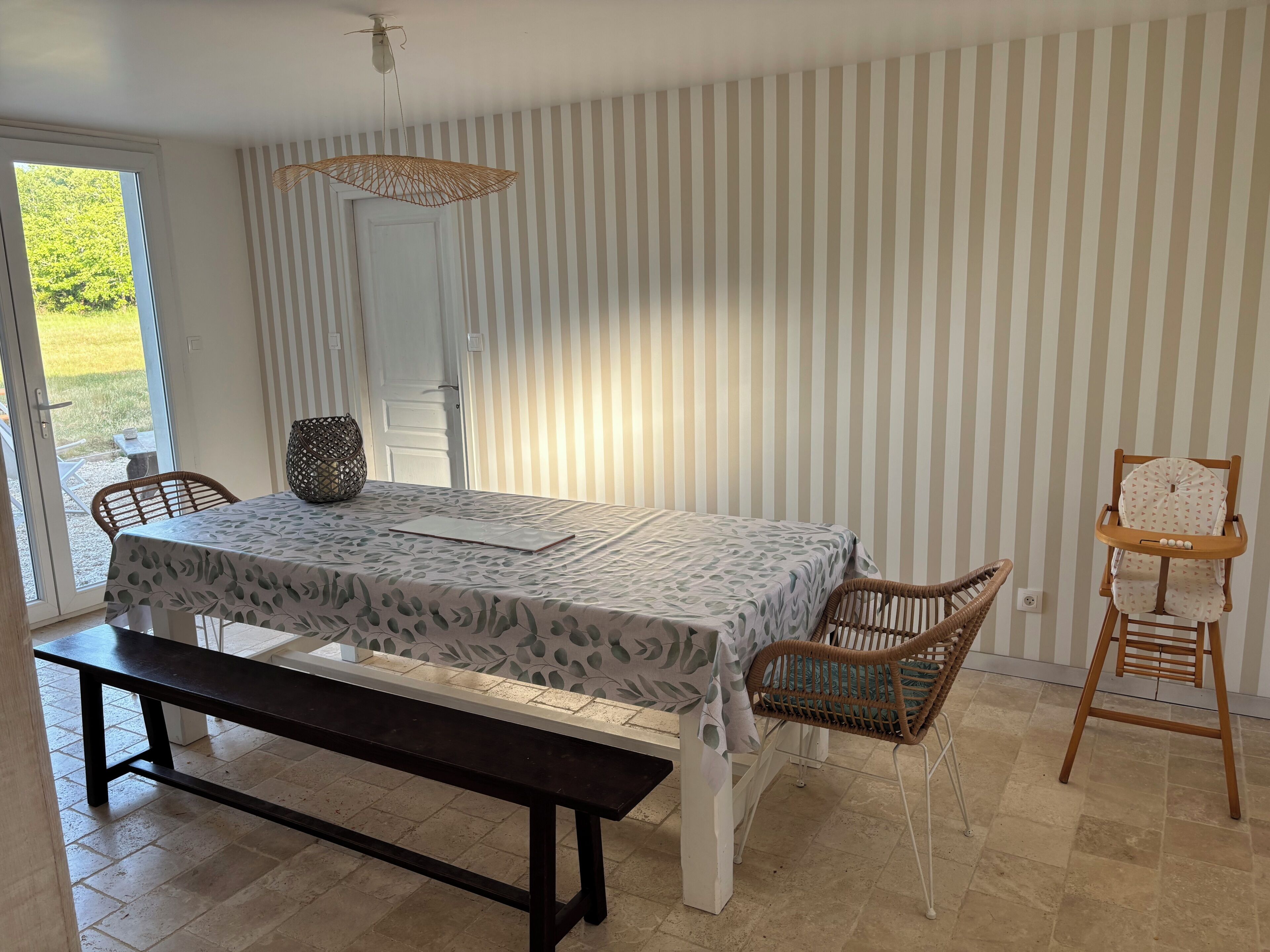 En matplats med ett bord, stolar, en bänk, en hängande lampa och utsikt genom en glasdörr.