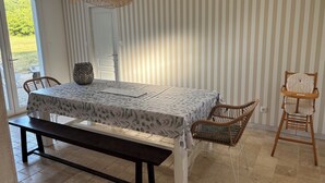 A dining area with a table, chairs, a bench, a hanging light fixture, and a view through a glass door.