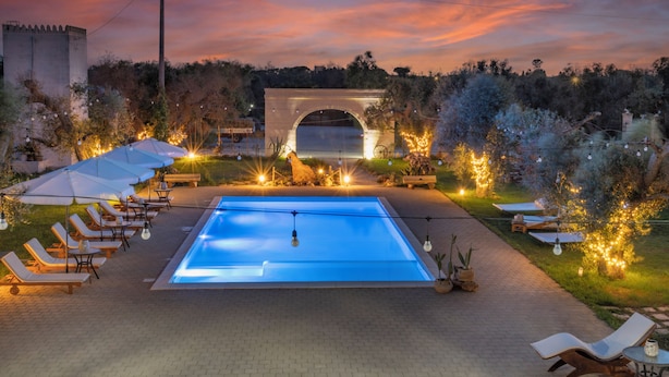 A swimming pool with lounge chairs and umbrellas, surrounded by greenery and a stone archway. - Oasis of peace and serenity, nestled in the countryside. (Mesagne)