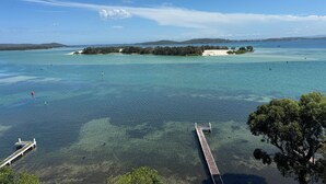 Paisaje costero con aguas cristalinas, un muelle y una pequeña isla con árboles.