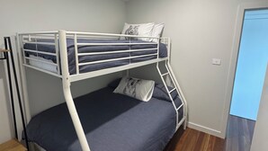 Una cama litera con piso de madera, una mesita y una puerta.