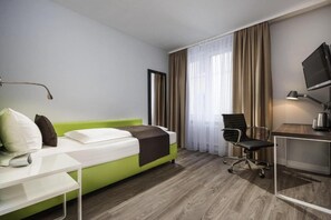 Ein Hotelzimmer mit Bett, Schreibtisch, Stuhl, Fernseher und einem Fenster mit Vorhängen.