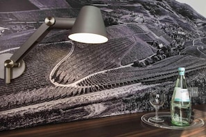 Ein Tisch mit einer Gerolsteiner Weinflasche, einem Weinglas und einer Lampe auf einer Tischdecke mit einem Motiv von Weinbergen.